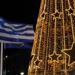 A glowing Christmas tree with Greek flags waving at night, creating a festive atmosphere.